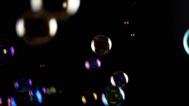 Renkli sabun köpükleri ıssız Kara Arkaplanda, boşlukta uçuyor. Renkli ışıklar. Birçok gökkuşağı şeffaf kabarcıkları rastgele döner, yüzer, düşer, patlar. Bulanık hareket. Seçici odaklanma. Soyut.