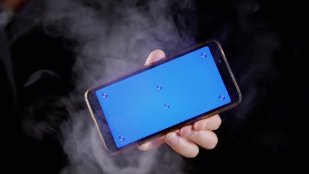 Hand Holding Mobile Phone Blue Screen Black Background Smoke Hand — Stock Video