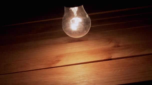 One Swinging Hanging Glowing Incandescent Light Bulb Wooden Background Dusty — Stock Video