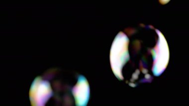 Bir sürü renkli sabun köpüğü kara zeminde uçuşuyor. Üfleme. Sıçra, köpük. Hızlı bulanık hareket. Soyut, enerjik küreler. Seçici odaklanma. Boşluk. Siyahta izole edilmiş. Işıklandırma.