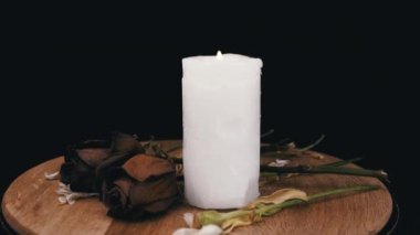 Yanan Beyaz Mum ve Kurumuş İki Gül Siyah Arkaplanda Dönüyor. Uzayı kopyala Kurumuş çiçek tomurcuklarının bileşimi. Ölüm kavramı, üzüntü, üzüntü, keder. Ölüm yıldönümü. Tahta..