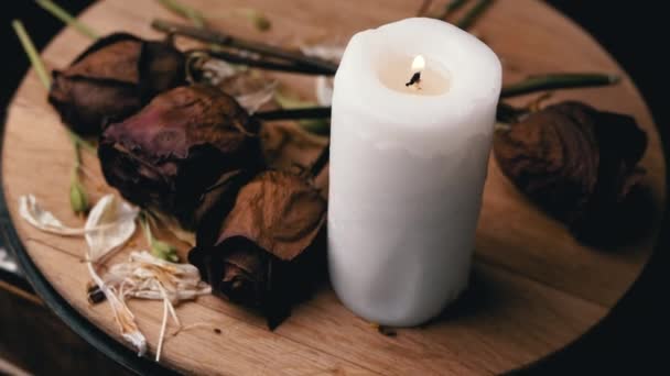 燃烧的白色蜡烛和四个枯干的玫瑰在黑色背景下旋转 干花芽的组成 悲伤的概念 死亡纪念日 木板板 — 图库视频影像