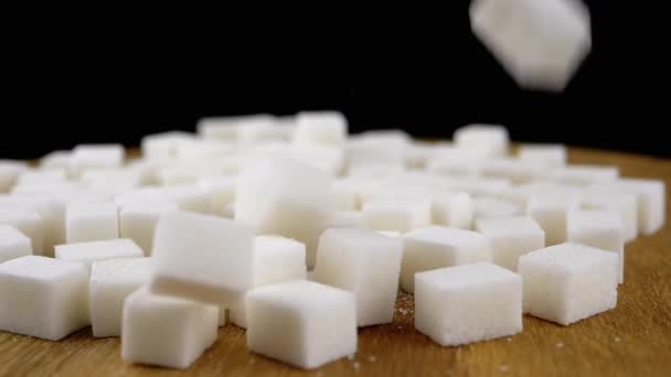 白砂糖のキューブは 回転木製の背景にある砂糖の山に落ちます クローズアップ テクスチャ 抽象的な背景 洗練された砂糖 パーティクルズ 糖尿病について 木の茶色の背景 スローモーション — ストック動画