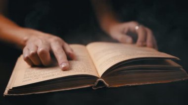 Gecenin karanlığında, dumanlı bir odada kitap okuyan kız. Duman bulutları. Kapatın. İçeride sigara içmek. Bir kadın parmağını kitabın sarı sayfalarında gezdiriyor. Gizemli bir atmosfer. Siyah arkaplan.