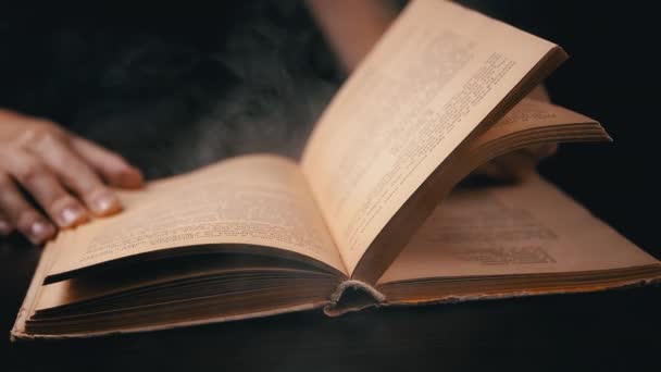 イギリス人 Kamenskoye 2023 閉じる スモーキーな部屋の古い本のページをガールフリップ 屋内で喫煙する 夜に面白い本を読んでいる 神秘的な雰囲気 ブラックバック — ストック動画