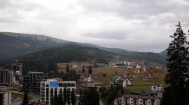 Sonbaharda Bukovel 'de tatil. Karpatlar 'ın panoramik manzarası, köy, modern otellerin çatıları, binalar. Altyapı tesisleri, kafeler, restoranlar. Tepeler, sis. Bulutlu. Kayak kaldırma.
