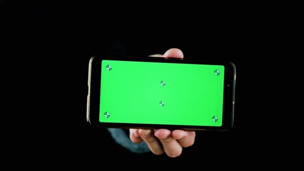 手拿着手机 黑色背景上有绿色屏幕 智能手机有一个空白的绿色屏幕 模拟了 复制空间 深色背景 — 图库视频影像
