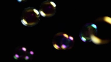 Renkli sabun köpükleri ıssız Kara Arkaplanda, boşlukta uçuyor. Renkli ışıklar. Birçok gökkuşağı şeffaf kabarcıkları rastgele döner, yüzer, düşer, patlar. Bulanık hareket. Seçici odaklanma. Soyut.
