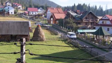 BUKOVEL, UKRAINE, 2023: Minibus Dağlardaki Kırsal Yol Geçidi Kır Evleri 'nden geçiyor. Orman ve tepeler arasında ahşap evler ya da kulübeler. Sonbahar ormanı arka planı, çimen. Kırsal.