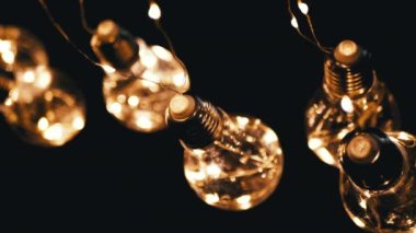 Birçok Asılı Parlayan Vintage Edison ampulleri Siyah Arkaplanda. Üst Manzara. Ilık ışık. Doku, yapı. Kürek çek. Dekoratif klasik elektrik ampulleri, retro tarzı çelenkler mekanı aydınlatıyor.