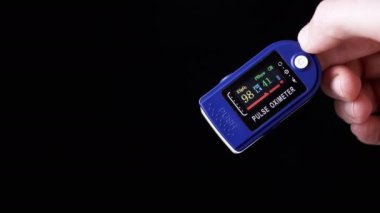 Kadın, Nabız ve Oksijen Doygunluğunu Evde Nabız Oksimetresi kullanarak Ölçüyor. Yakın plan. Siyah arka plan. Cihazın üzerinde sensörler ve göstergeler olan bir arama. Kalp atışlarının, nabzının, kalp atışlarının ölçümü.