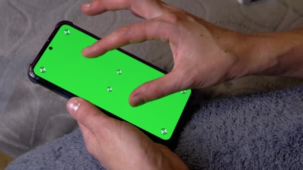 部屋の緑のスクリーンが付いているスマートフォンを握る女性手 指は携帯電話の画面を開けました コピースペースのためのクロマキーレイアウト ウィンドウの拡張 ソーシャルネットワーク ビデオコンテンツ インターネットを見る — ストック動画