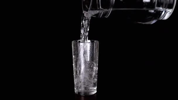 在黑色背景的卡拉菲杯子里倒入干净的饮用水 孤立无援慢动作一股清凉的水流注入透明的玻璃杯中 溅满了水花 水花滴 — 图库视频影像
