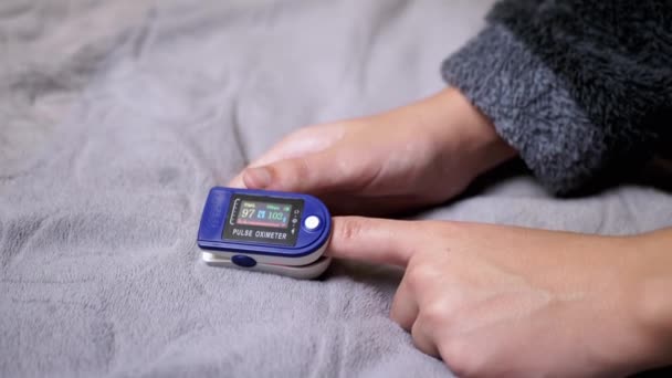 青少年在卧室用脉冲计测量脉冲电流和氧饱和度 孩子的手灰色背景 拨通装置上的传感器和指示器 脉搏的测量 该睡觉了 — 图库视频影像