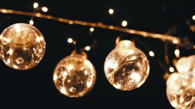 Birçok Asılı Parlayan Vintage Edison ampulleri Siyah Arkaplanda. Alt manzara. Ilık ışık. Doku, yapı. Kürek çek. Dekoratif klasik elektrik ampulleri, retro tarzı çelenkler mekanı aydınlatıyor.