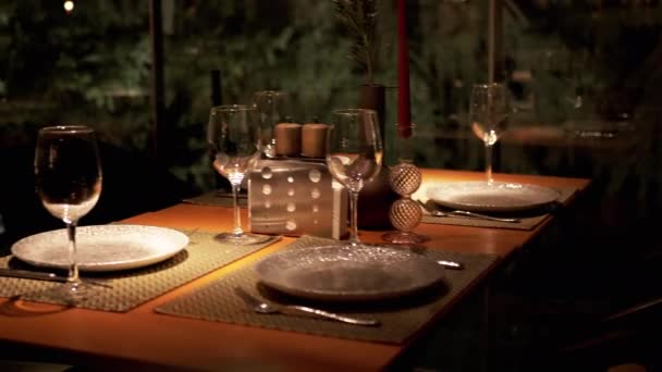 在舒适浪漫的夜晚氛围中的豪华餐厅里享用餐桌 空盘子 玻璃杯放在桌上 为四个人准备了美味的烛光晚餐 闪烁着温暖的光芒 从窗口看森林 — 图库视频影像
