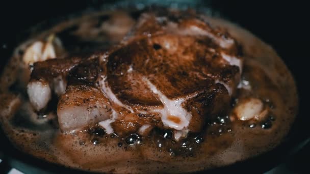 クローズアップ ボーンにポークステーキのジューシーなピース 沸騰油でフライパン テクスチャー 茶色のクリスピーな地殻 ニンニク スパイスで肉ステーキを調理する ファーム スローモーション 美味しいディナー — ストック動画