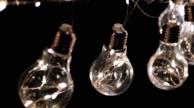 Parlak Vintage Edison Ampulleri Siyah Arkaplanda Tavanda Asılı. Arka arkaya. Ilık ışık. Kablo. Noel süslemeleri, klasik elektrik ampulleri, retro tarzı çelenkler mekanı aydınlatıyor.