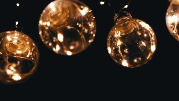 大量挂在黑色背景上的旧式爱迪生灯泡 底部的观点 装饰老式电灯泡 复古风格的花环照亮了整个空间 — 图库视频影像