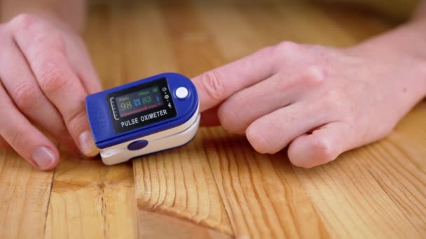 女人在家里用脉冲计测量脉冲电流和氧饱和度 木制背景 刻度盘装置上有传感器和指示器的刻度盘心率 心跳的测量 — 图库视频影像