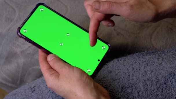 ベッドタイムの部屋の緑色のスクリーンとスマートフォンを握る女性の手 コピースペースのためのクロマキーレイアウト ニュースフィードをスクロールする指 指でスマートフォンのクロマティックスクリーン上のビデオ — ストック動画