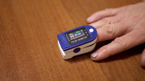 男性在家中使用脉冲血氧计测量脉搏和氧饱和度 木制背景 刻度盘装置上有传感器和指示器的刻度盘心率 心跳的测量 — 图库视频影像