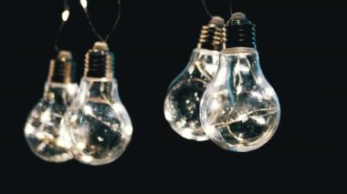 Birçok Sallanan Parıldayan Vintage Edison ampulleri Kara Arkaplanda. Ilık ışık. Noel süslemeleri, klasik elektrik ampulleri açılıp kapanıyor, retro tarzı çelenkler mekanı aydınlatıyor.