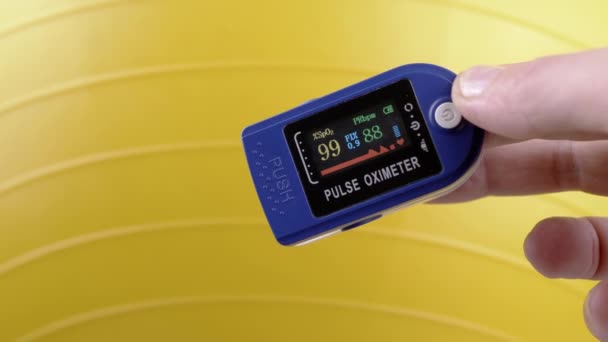 運動中にパルス近似体を使用して脈拍と酸素の土壌を測定する手 クローズアップ デバイス上のセンサーとインジケータをダイヤルします 心拍数の測定について イエローバック フィットネスボール — ストック動画