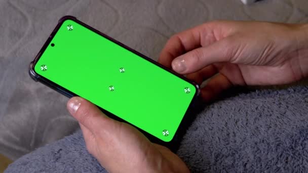 ベッドタイムの部屋の緑色のスクリーンとスマートフォンを握る女性の手 コピースペースのためのクロマキーレイアウト ニュースフィードをスクロールする指 指でスマートフォンのクロマティックスクリーン上のビデオ — ストック動画