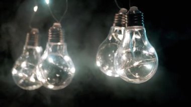 Smoke on a Black Background 'da Parlayan Vintage Edison ampullerini asmak. Ilık ışık. Doku, yapı. Noel süslemeleri, klasik elektrik ampulleri, retro tarzı çelenkler mekanı aydınlatıyor.