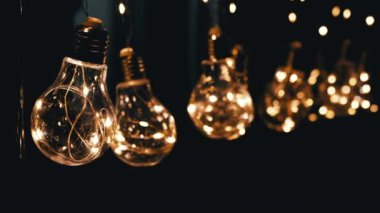 Birçok Sallanan Parlayan Vintage Edison ampulleri Siyah Arkaplanda. Ilık ışık. Doku, yapı. Kürek çek. Dekoratif klasik elektrik ampulleri, retro tarzı çelenkler mekanı aydınlatıyor.