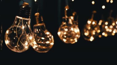 Birçok Sallanan Parlayan Vintage Edison ampulleri Siyah Arkaplanda. Ilık ışık. Doku, yapı. Kürek çek. Dekoratif klasik elektrik ampulleri, retro tarzı çelenkler mekanı aydınlatıyor.