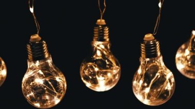 Birçok Asılı Parlayan Vintage Edison ampulleri Siyah Arkaplanda. Üst Manzara. Ilık ışık. Doku, yapı. Kürek çek. Dekoratif klasik elektrik ampulleri, retro tarzı çelenkler mekanı aydınlatıyor.