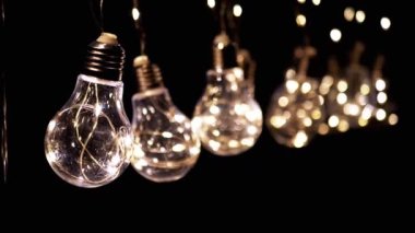 Birçok Sallanan Parlayan Vintage Edison ampulleri Siyah Arkaplanda. Ilık ışık. Doku, yapı. Kürek çek. Dekoratif klasik elektrik ampulleri, retro tarzı çelenkler mekanı aydınlatıyor.