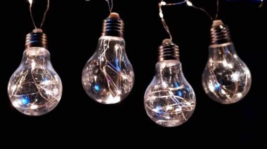 Birçok Sallanan Parıldayan Vintage Edison ampulleri Kara Arkaplanda. Arka arkaya. Noel süslemeleri, klasik elektrik ampulleri açılıp kapanıyor, retro tarzı çelenkler mekanı aydınlatıyor.