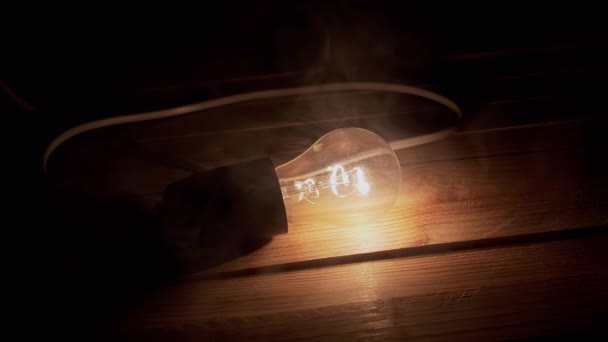Одна Светящаяся Лампочка Накаливания Проволокой Лежит Деревянном Столе Дыму Текстура — стоковое видео