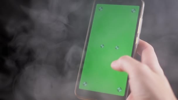 在黑烟中手握带有绿色屏幕的手机 手指用彩色键触摸空白触摸屏智能手机 制造商 空荡荡的地方浓浓的烟云 — 图库视频影像