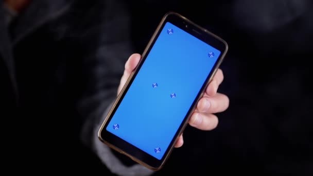 在黑烟中手握带有蓝色屏幕的手机 手动旋转一个带有空白屏幕的智能手机 彩色键 在浓密的烟雾中模拟在空旷的空间 — 图库视频影像