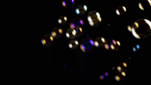 彩色的肥皂泡在空旷的空间中 在孤立的黑色背景下飞舞 金色的灯许多彩虹透明气泡随机旋转 模糊的动议 有选择的重点 — 图库视频影像