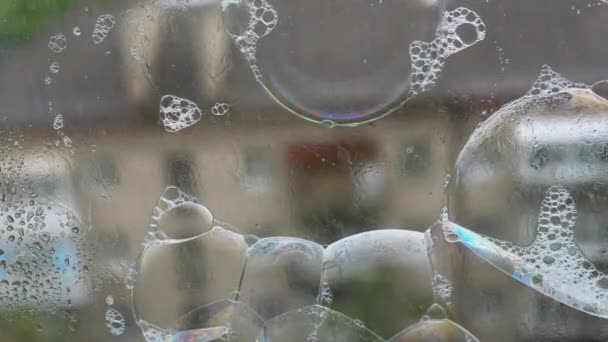 湿淋淋的窗户表面有许多粘稠的彩色肥皂泡 在玻璃表面喷出泡沫的肥皂彩虹泡沫 外面下着雨 — 图库视频影像