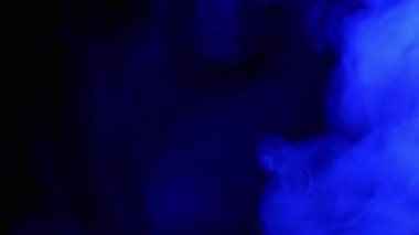 Mavi Duman 'ın patlaması ya da Siyah Bulanık Arkaplanda Buhar. Flaş. Soyut. Yan görüş. Yumuşak dumanlar ya da boş uzayda kaotik bir şekilde buhar karışımı. Parçacık patlaması, parlak ışık. Yavaş çekim.