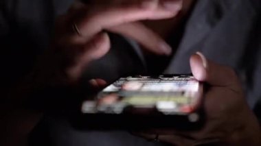 Karanlık bir ortamda parlak bir akıllı telefon ekranını kaydıran ellerin yakın çekimi. Teknoloji ve mobil uygulama ile ilgili projeler için ideal.