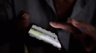 Sönük bir ayarda akıllı bir telefondan haber akışında süzülen ellerin yakın çekimi. Ekrandaki ışık içerikte gezinirken parmakları aydınlatır. İlgili projeler için mükemmel