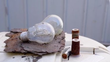 İki eski ampul paslı bir yüzeyde duruyor, çürüme ve eskimişliği resmediyorlar..
