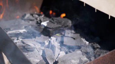 Metal bir ızgarada kömür yanıyor, alevler ve duman yükseliyor, sıcaklık ve beklenti hissi uyandırıyor, açık hava yemekleri, barbekü ve yaşam tarzı projeleri için mükemmel..