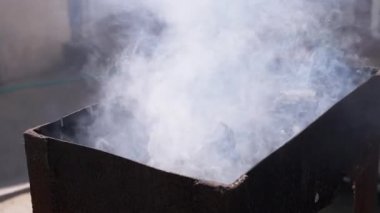 Alev alev yanan kömürlerle dolu metal bir biberondan yükselen beyaz duman, barbekü için bir beklenti sahnesi yaratıyor..