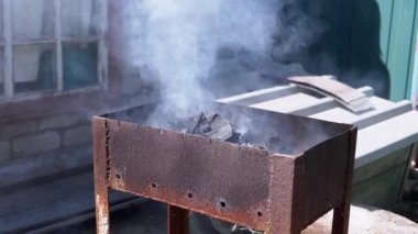 Duman çıkaran kömürlerle paslı bir brazier 'ın yakın çekimi, beyaz duman yaymak, açık havada et pişirmek için hazırlık. Barbekü, yemek pişirme ve yaz tatili projeleri için mükemmel..