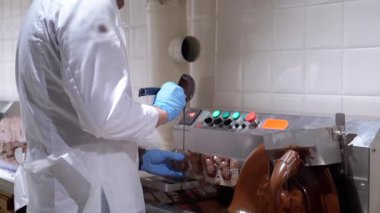 Beyaz üniformalı ve mavi eldivenli bir şekerci şeker kalıbını şekerleme fabrikasında koyu sıvı çikolatayla doldurur. Çikolata üretim süreci, tatlı gıda endüstrisi.