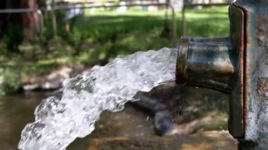Su eski paslı bir borudan bir gölete akar ve dalgalanmalar yaratır. Ağır çekimde yakın çekim. Suyun korunumu ve kirliliğini gösterir.