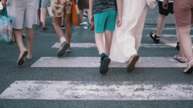 Yaya geçidinde yürüyen insan bacakları, işlek bir sokak manzarası, yaz günü. Bacaklara ve ayakkabılara, asfalt dokusuna, beyaz çizgilere odaklan..